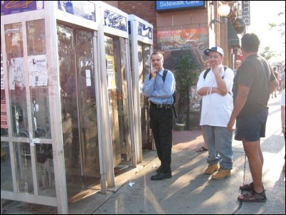 Bored (but good natured!) people wait at the phone booth.